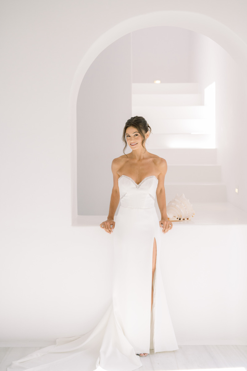 Elegant bride in white gown posing in a white room with architectural lines at Mykonos wedding.